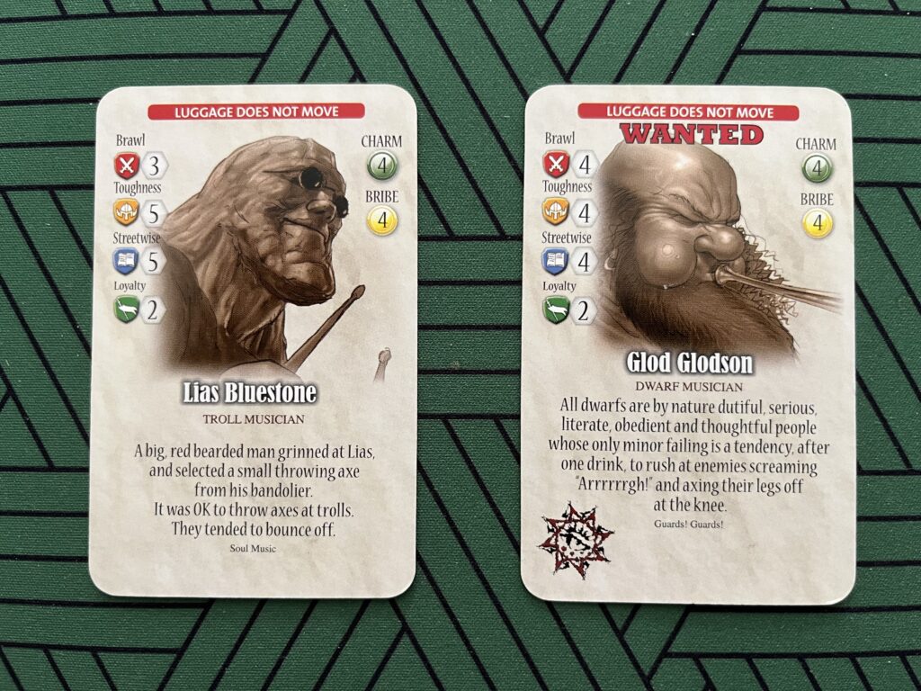 A photo of two volunteer cards from the Guards! Guards! board game: Lias Bluestone and Glod Glodsson, both characters from Soul Music. Lias’ card has text from his book describing a man getting out an axe to throw at him. Glod’s card has a quote about the nature of dwarfs from Guards! Guards!